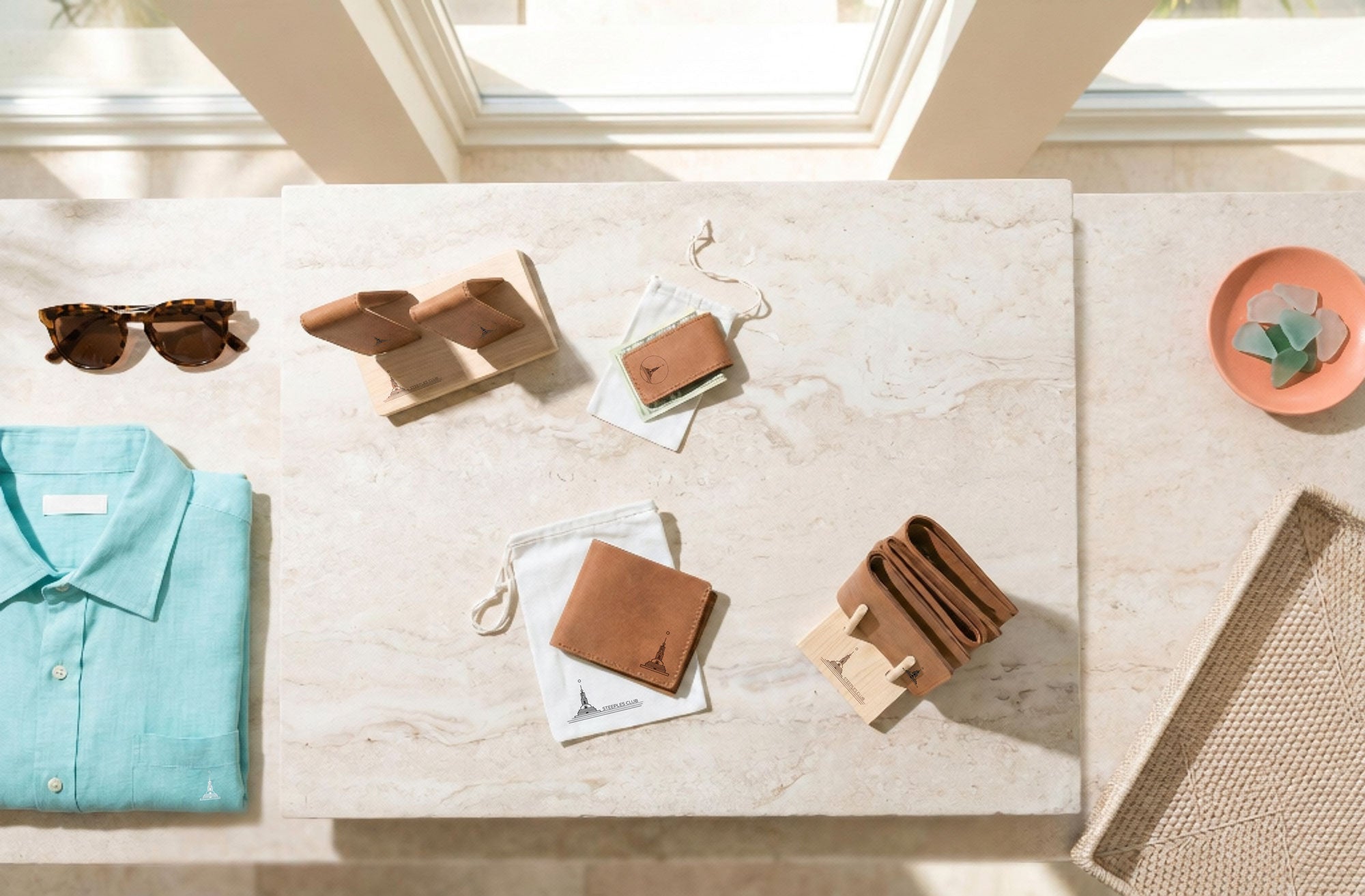 Collection of leather items including a wallet, cardholder, and sunglasses on a light surface with a window in the background.