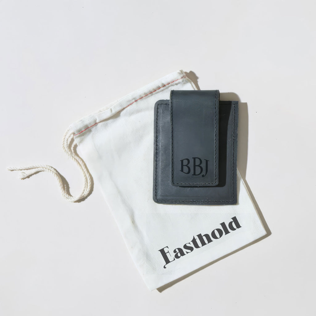 Black leather money clip cardholder with 'BBJ' initials on a branded white dst bag