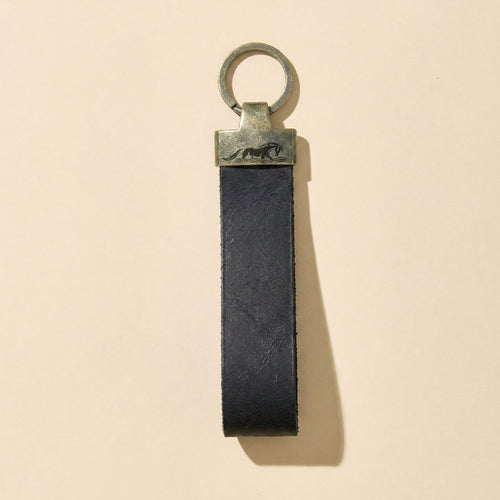 Black leather keychain with logo engraving on metal ring on a beige background