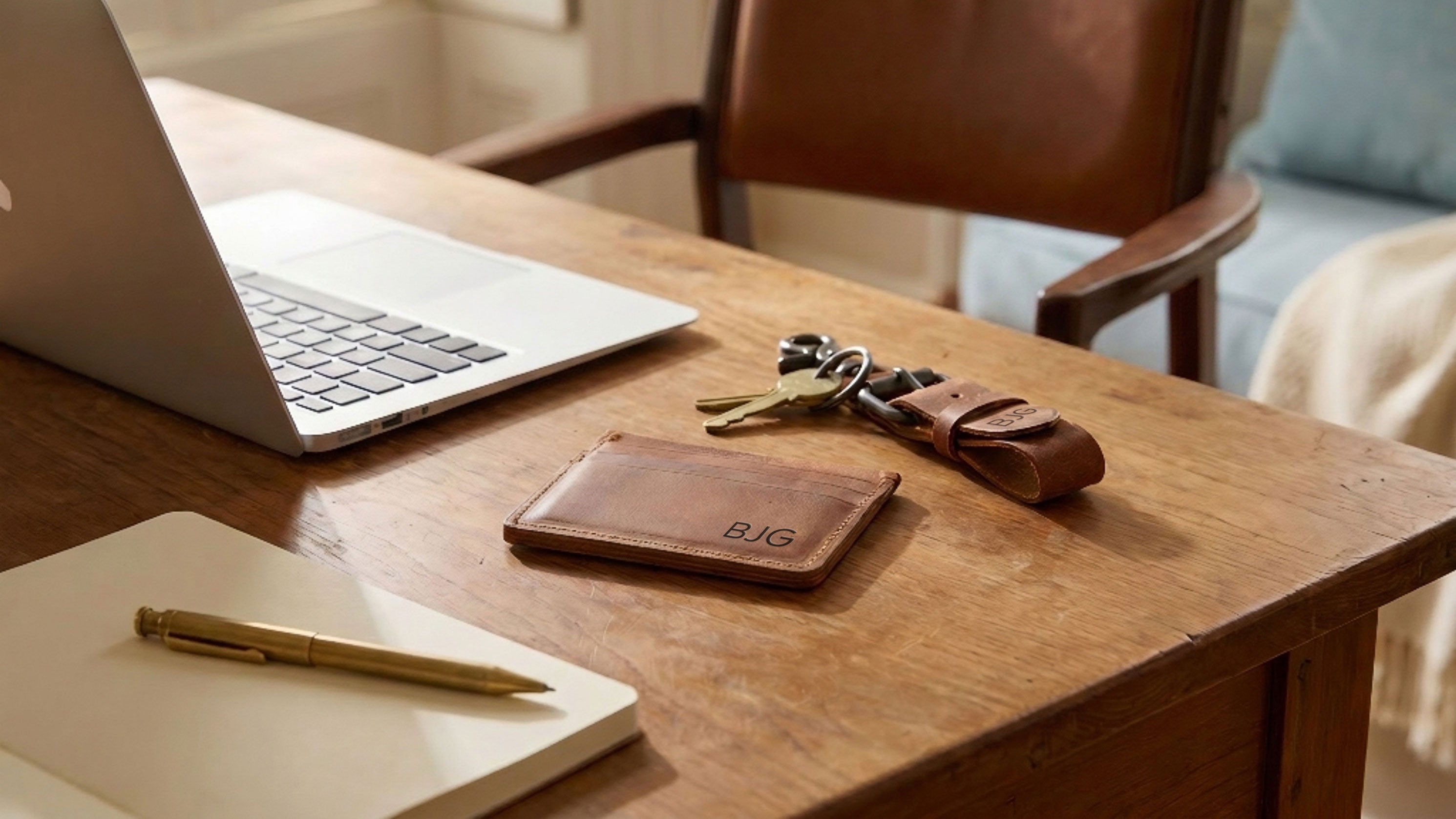 Laptop, notebook, pen, leather wallet, and keys on a wooden desk.
