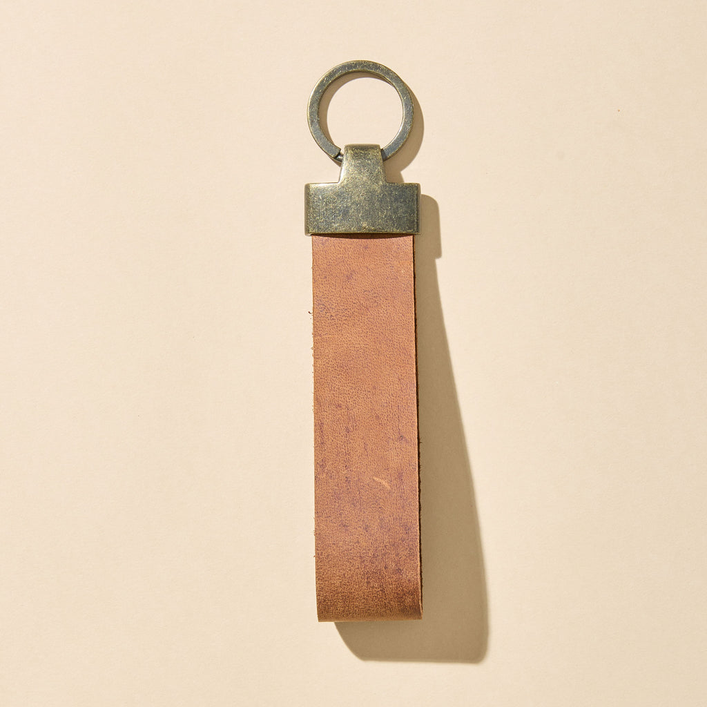 Brown leather keychain with metal ring on a beige background