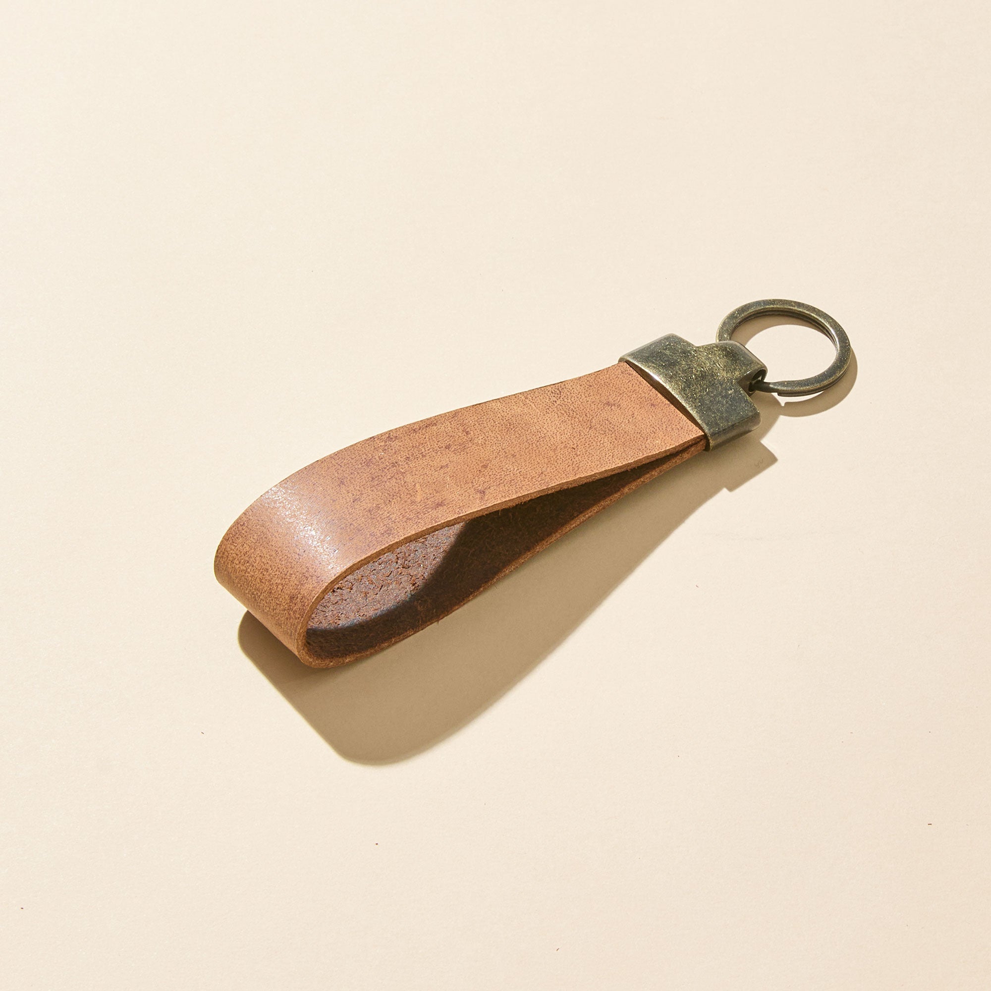 Brown leather keychain with brass ring on a beige background