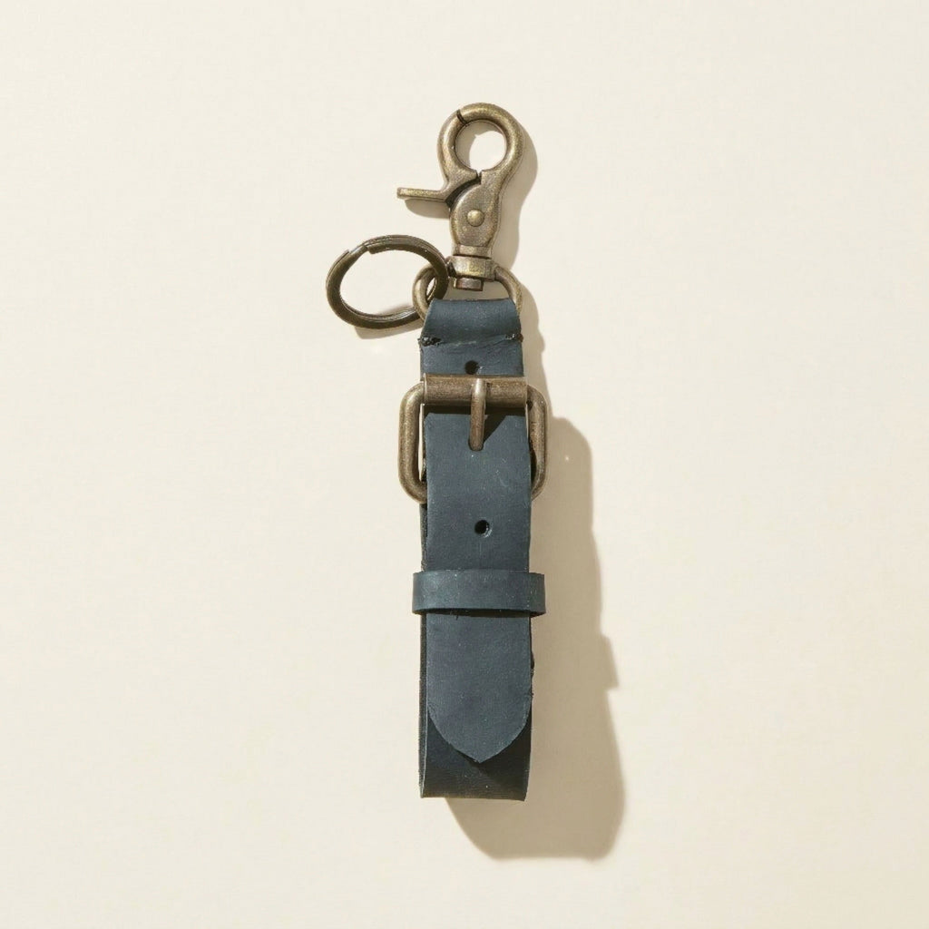 Black leather keychain with metal clasp on a beige background