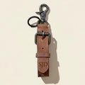 Brown leather keychain  with engraved initials with metal clasp on a beige background