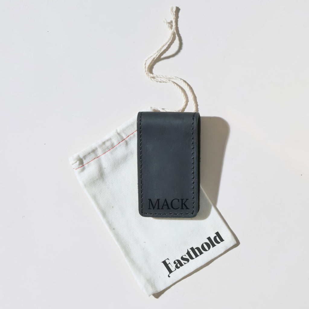 Black leather money clip with 'MACK' Monogrammed sitting on a white drawstring bag with 'Easthold' branding.