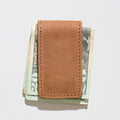 Brown leather money clip holding U.S. dollar bills on a light gray background